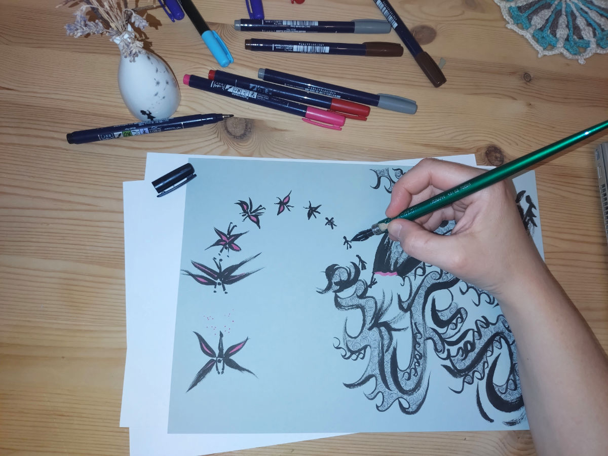 Die Hand von Birgit Sailer mit einer Feder in der Hand, wie sie eine Figur zeichnet