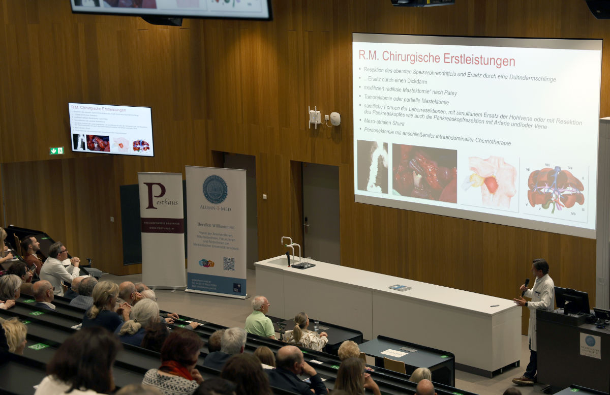 Stefan Schneeberger im weißen Mantel hält einen Vortrag mit PowerPoint Folien.
