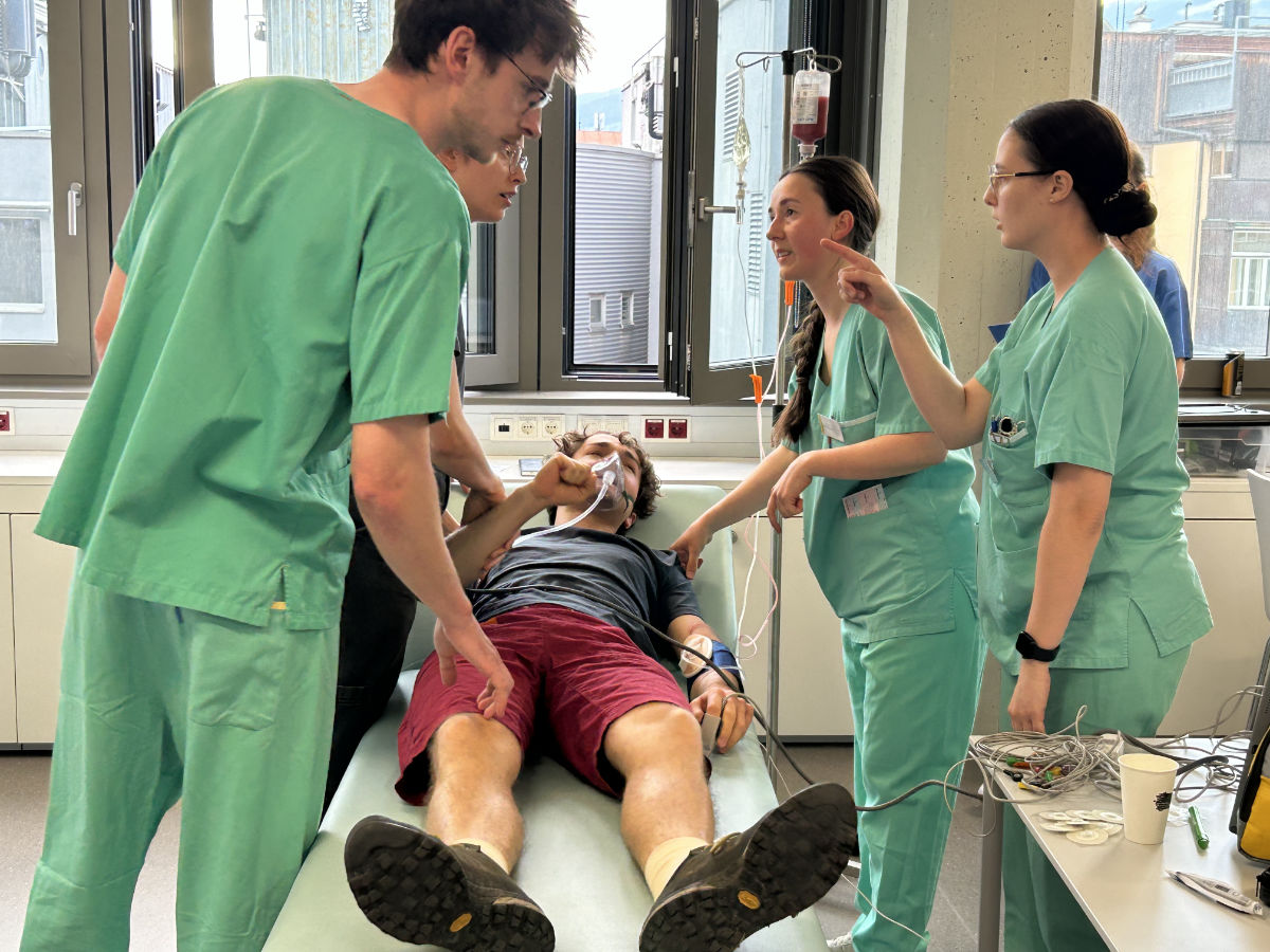 Eine Gruppe von vier Studierenden steht um einen Patienten herum, der auf einer Liege liegt.