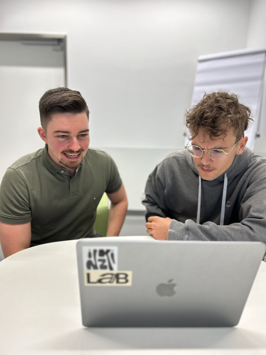 Friedrich Völkl und Ben Hofbauer sitzen am Laptop, Völkl schaut belustigt, Hofbauer skeptisch in den Bildschirm.